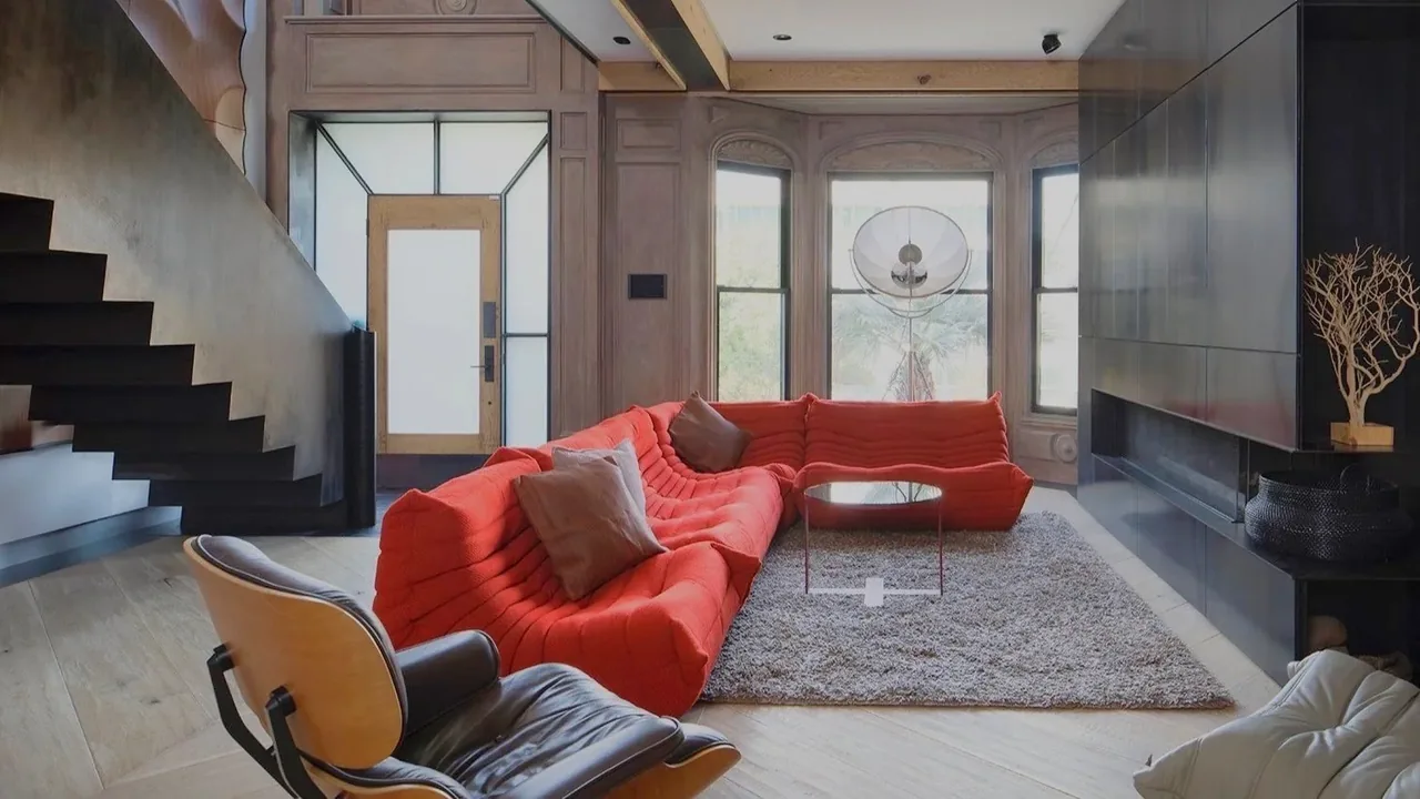 Living room featuring a bold red sectional sofa with a black leather lounge chair and large windows for natural light.