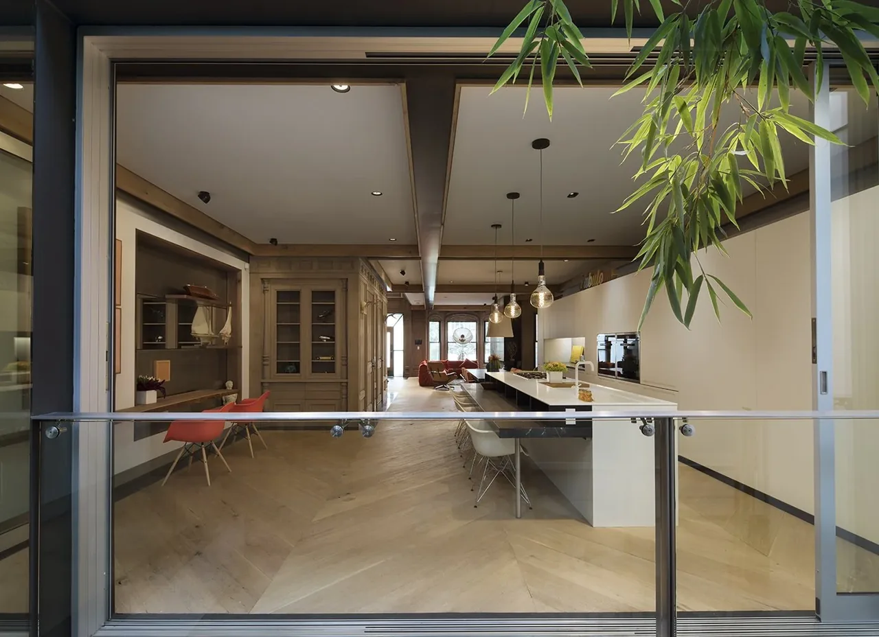 Modern kitchen and living area with patterned wood flooring and pendant lighting, featuring a long white kitchen island and red dining chairs.