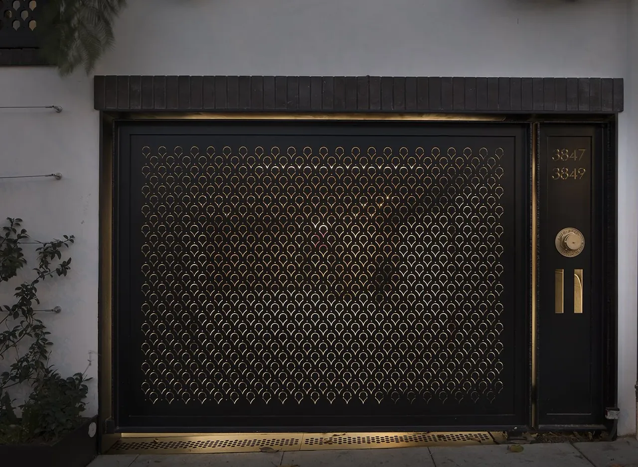 A black metal gate with a repeating circular pattern features gold accents and house numbers 3847 and 3849.