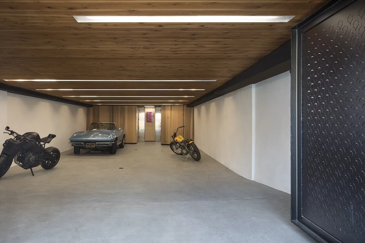 Garage space featuring wood ceiling panels with linear recessed lighting and concrete floor, housing a classic convertible and two motorcycles.