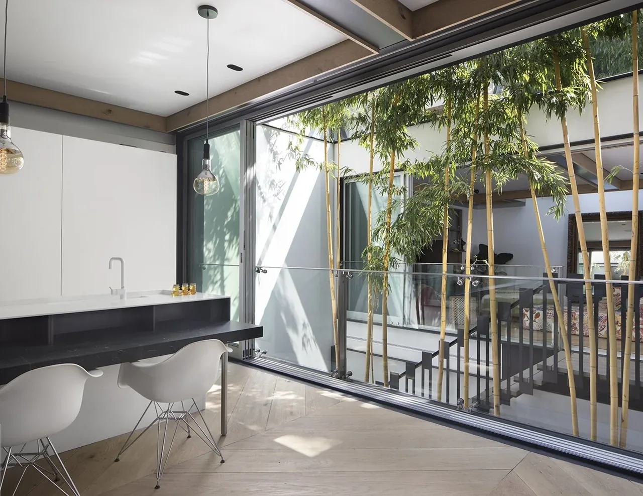 Kitchen with large glass wall overlooks an interior courtyard with bamboo plants and connects to the living and dining areas.