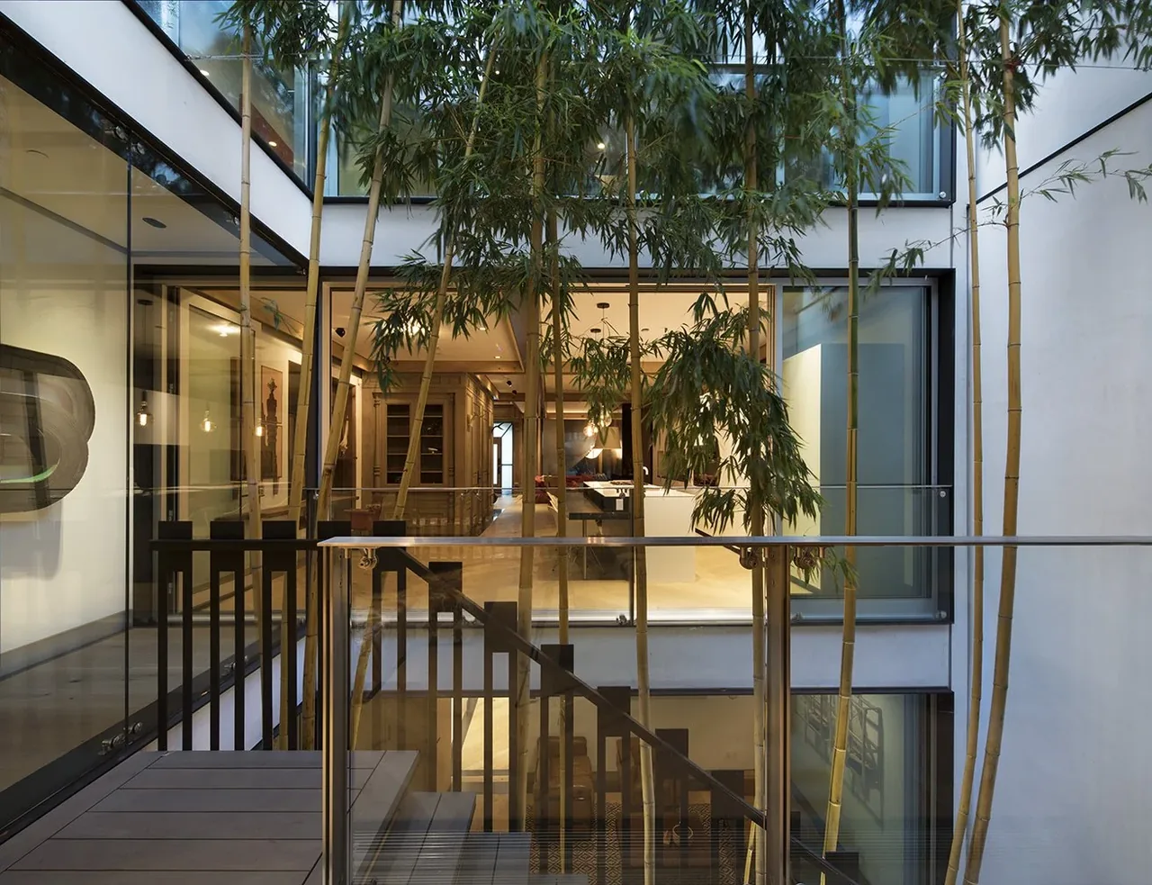 Interior courtyard with bamboo plants visible from a balcony featuring glass railing and metal handrails.