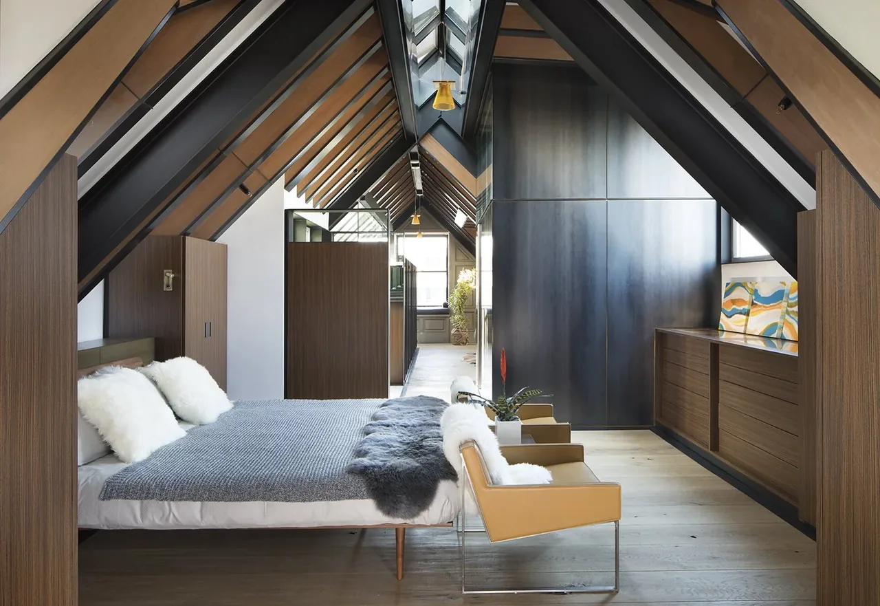 A bedroom with angled ceiling and sloped skylight ceiling featuring wood panel walls and custom cabinetry.