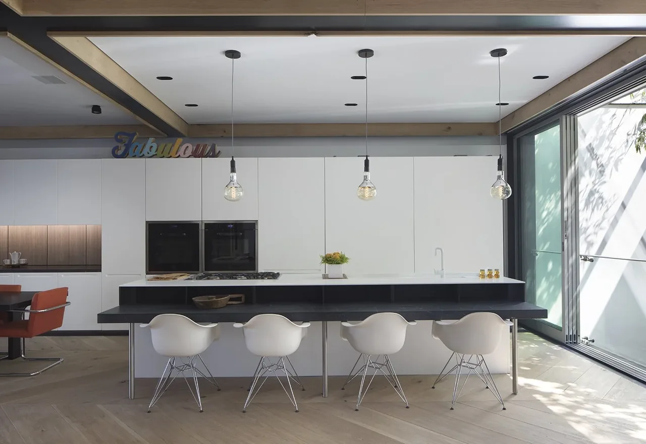 A kitchen with white cabinetry, black bar counter, pendant lights, and floor-to-ceiling sliding glass doors to the outside.