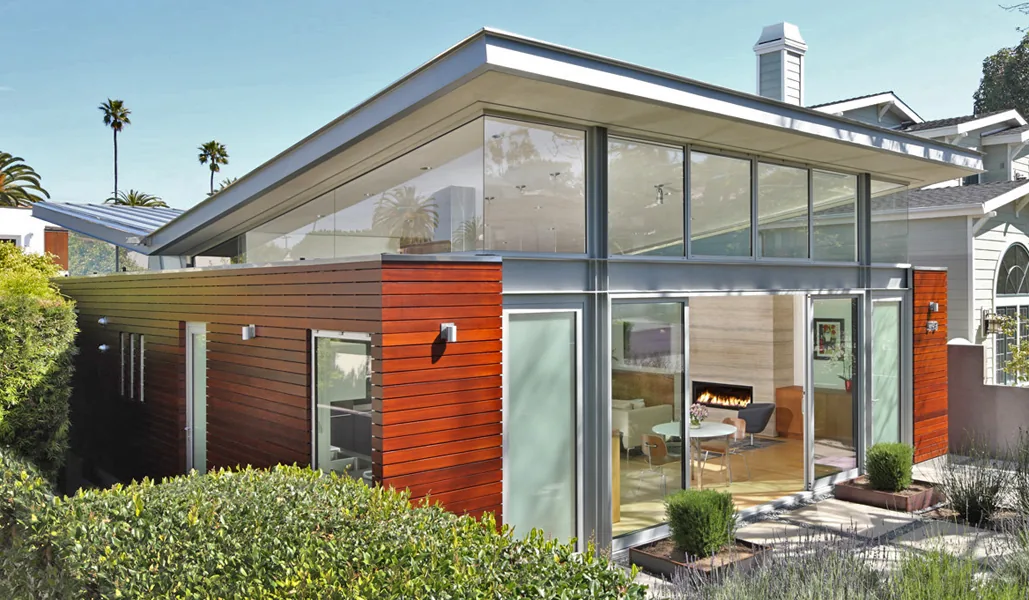 Exterior view of the Madans house by Dean Nota Architects showcasing glass walls and red wood siding under a slanted flat roof.