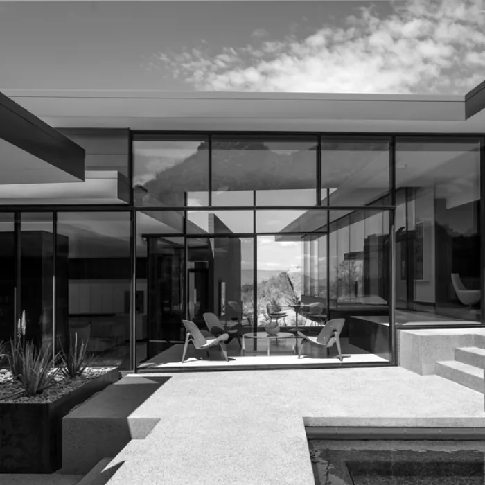 The desert platform project features large glass walls and an open patio with seating, showcasing mountain views.