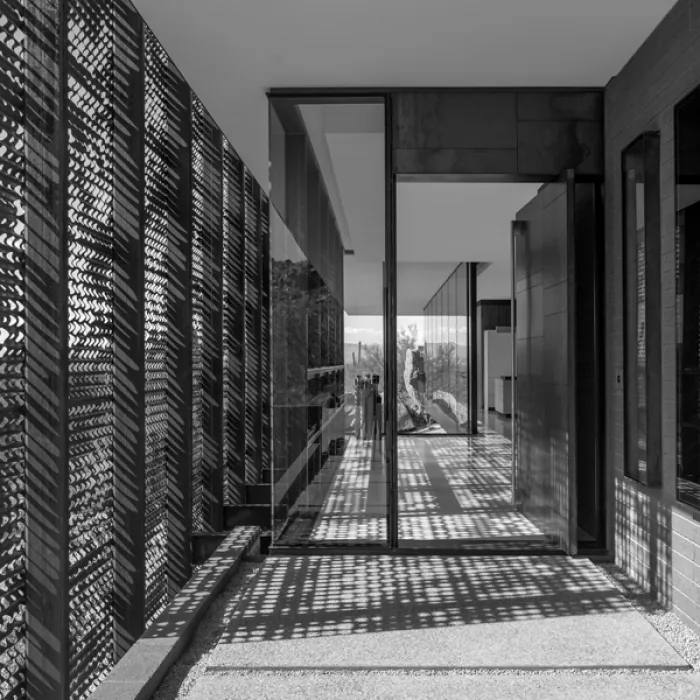 Exterior walkway featuring vertical metal slat screens and floor-to-ceiling glass wall panels with mountain views.