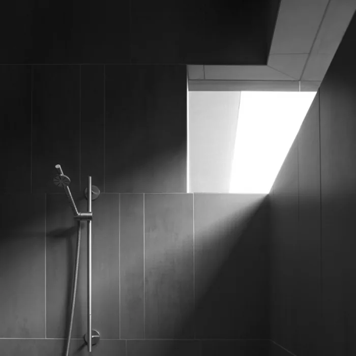 Shower with dark tile walls and a skylight illuminating the space.