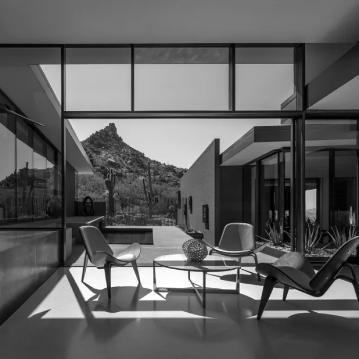 Interior seating area with glass walls offers a view of desert plants and a rocky hill outside.