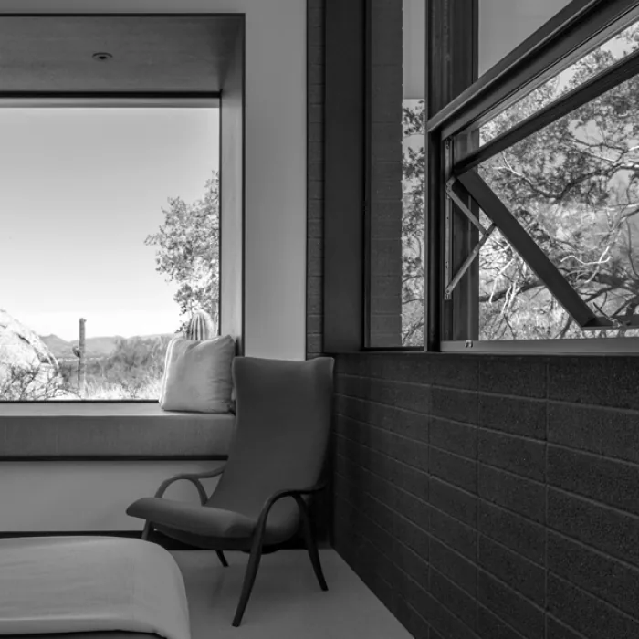 A sitting area with a lounge chair and window seat frames a view of the desert and rocky hills.