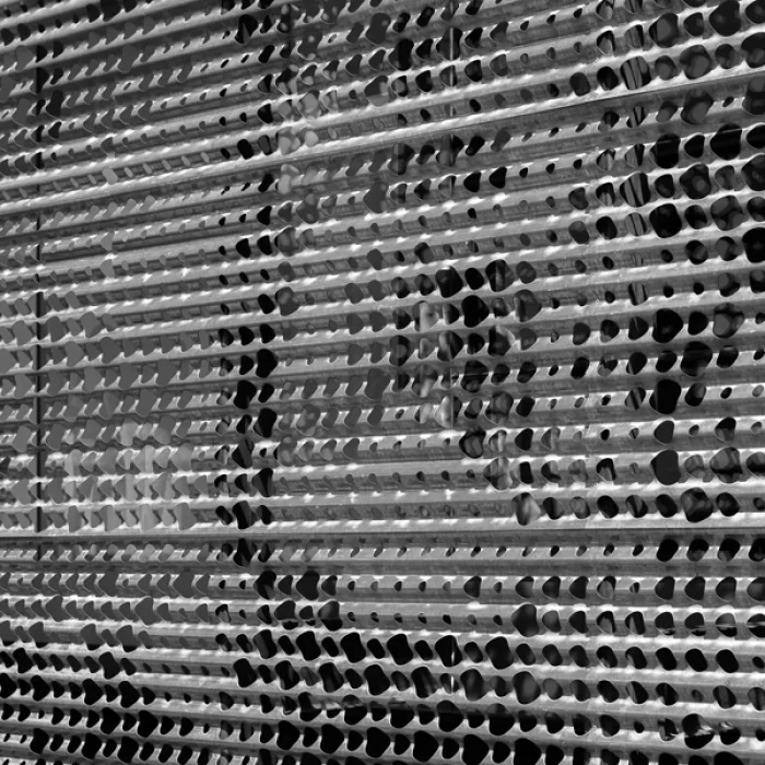 Metal slatted screen with punched hole design creating light and shadow patterns.