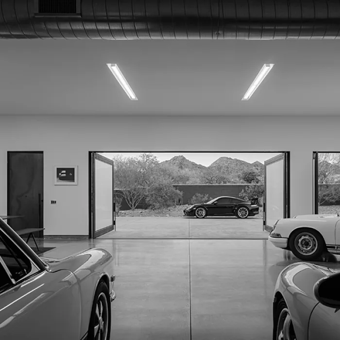 Garage interior with polished concrete floor, wood-framed glass doors open to a driveway with a black sports car visible.