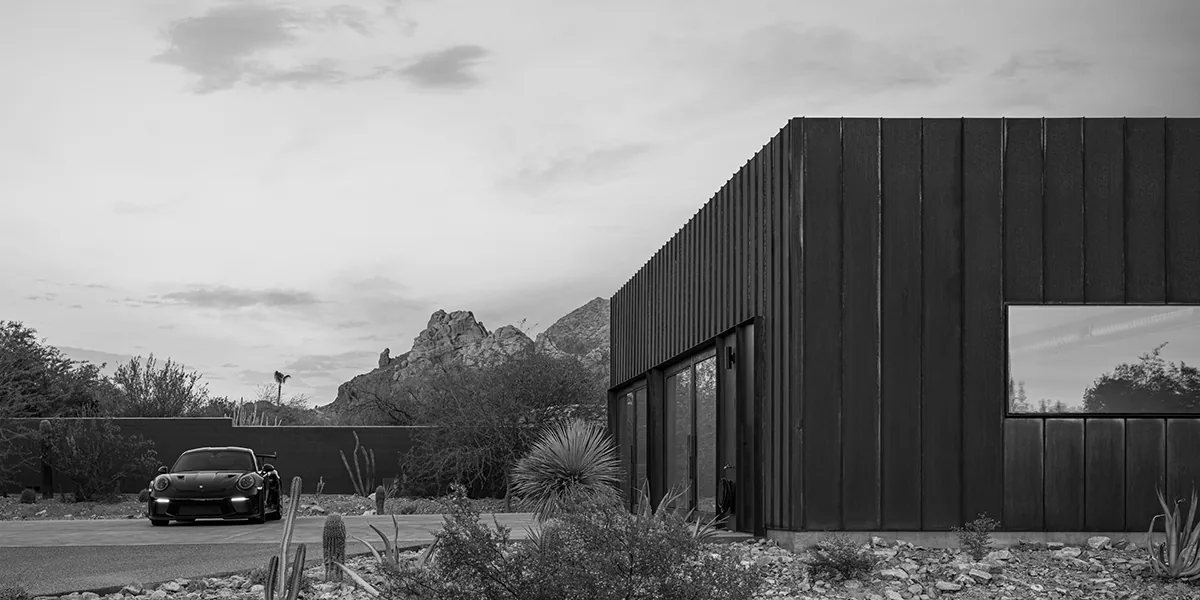 Modern garage clad in dark vertical metal panels with wood-framed glass doors and a black sports car parked in front.