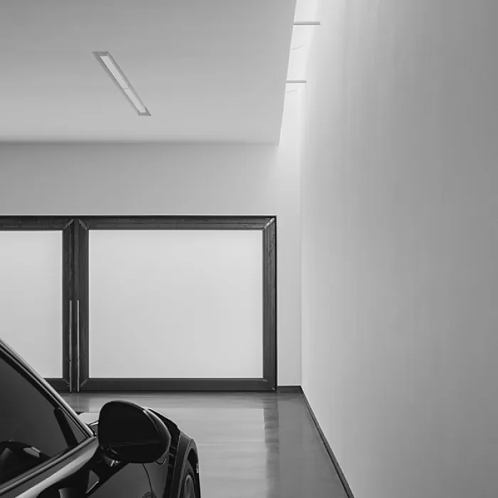 Minimalist garage interior with a black car, white walls, smooth floor, framed garage doors, and a narrow skylight.