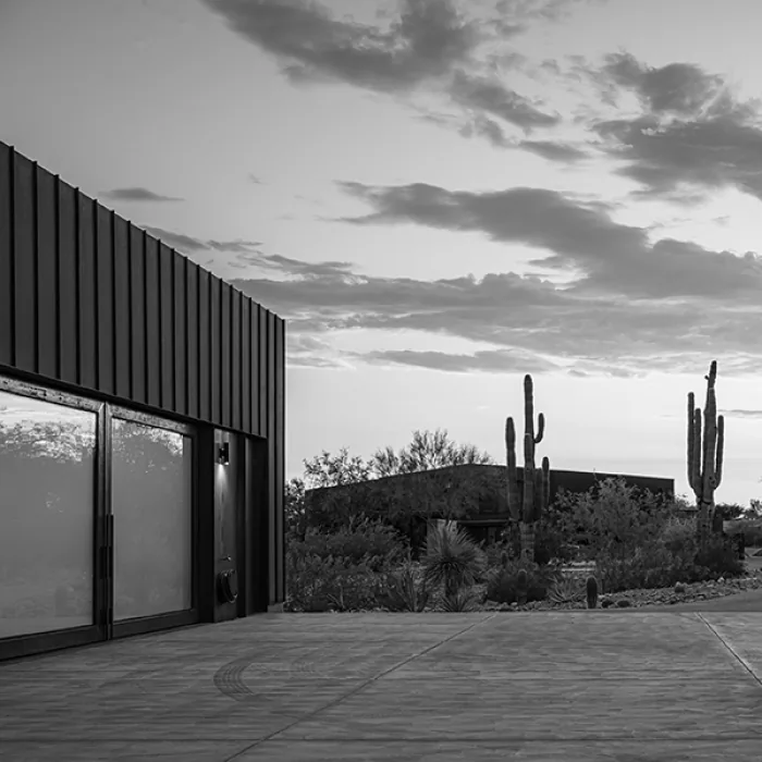 Modern garage with black metal siding and large wood-framed glass doors opening onto a concrete driveway.
