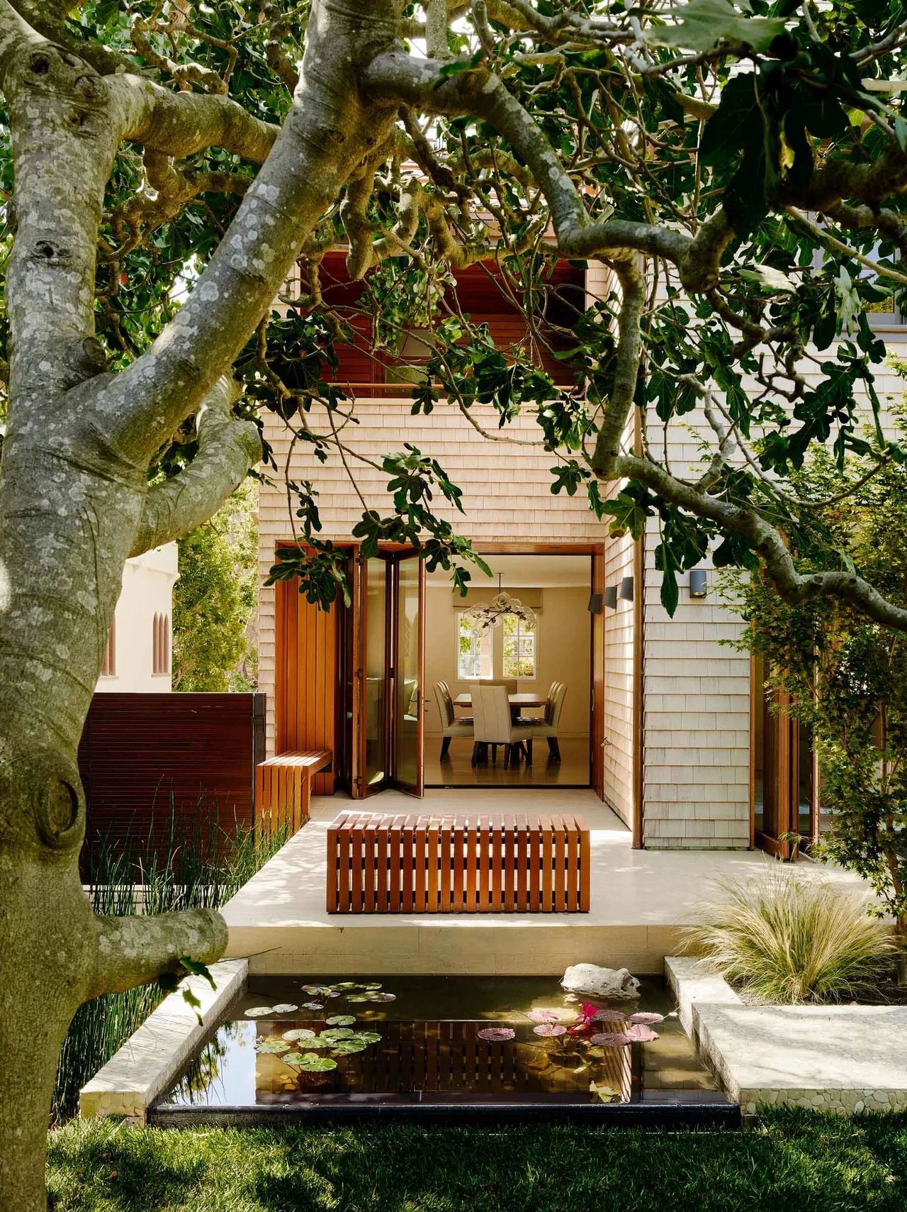 The Claremont Residence features an outdoor patio with a water lily pond and visible dining area inside through folding glass doors.