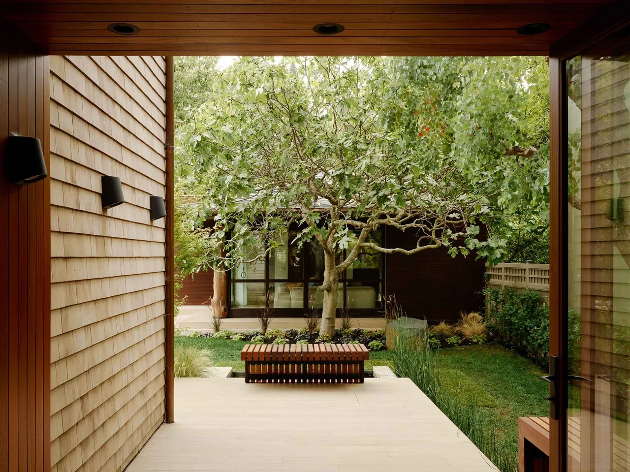 Outdoor living space with wooden siding, a bench, and a landscaped yard at the Claremont Residence.