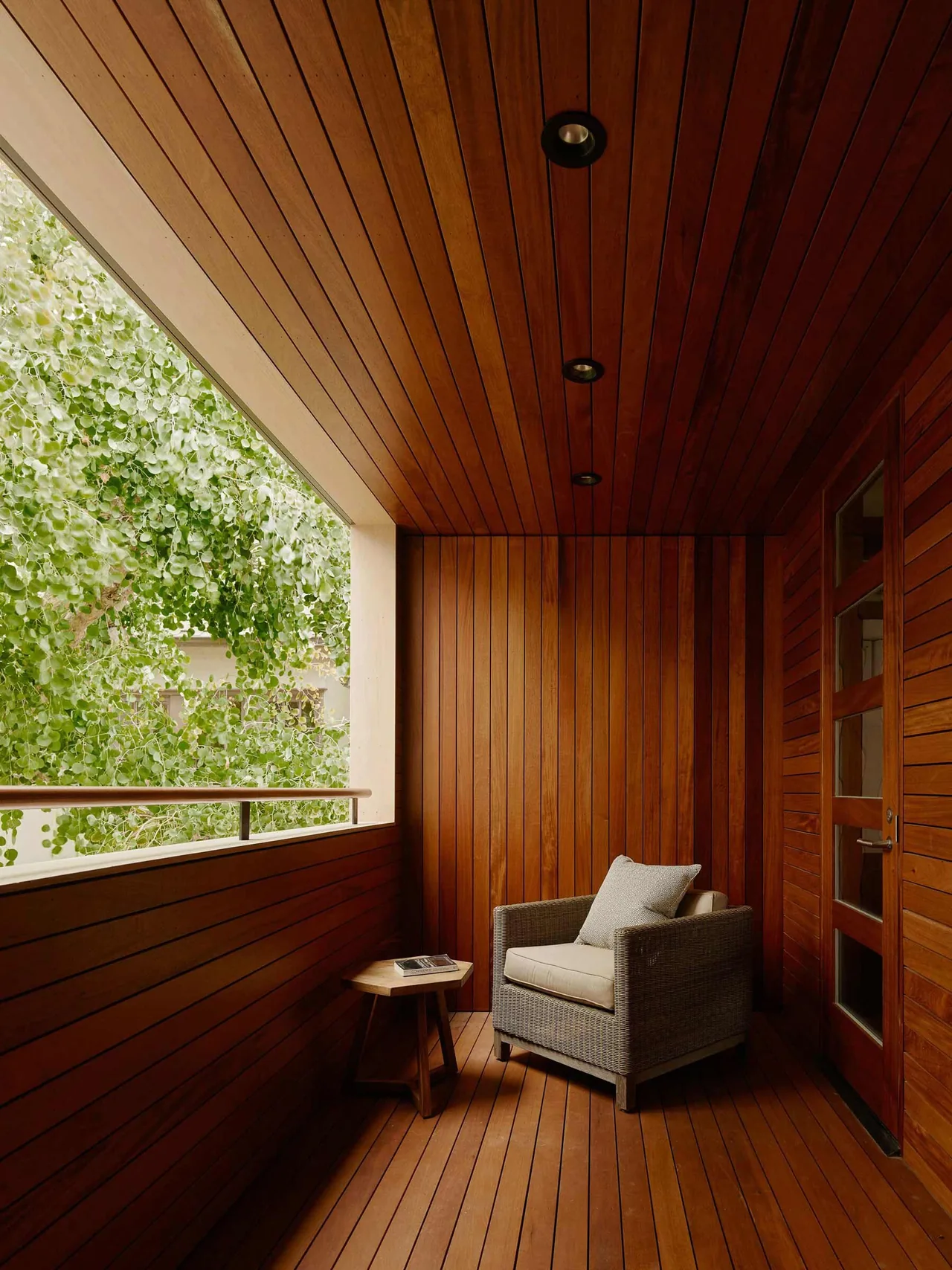 The Claremont Residence features a warm wood-paneled covered balcony with cozy seating and recessed lighting.