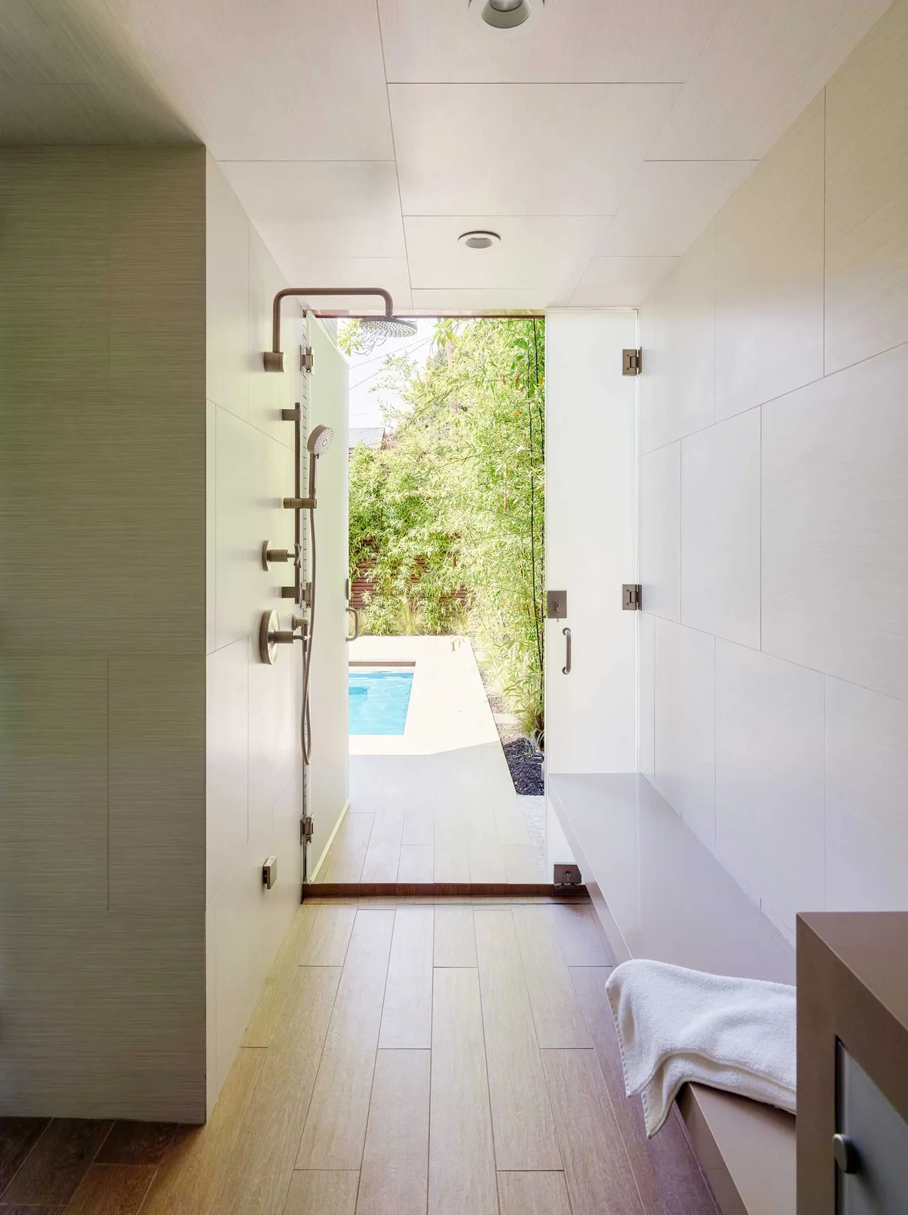 Shower area with wood-look tiles leads to an outdoor pool surrounded by greenery at Claremont Residence.