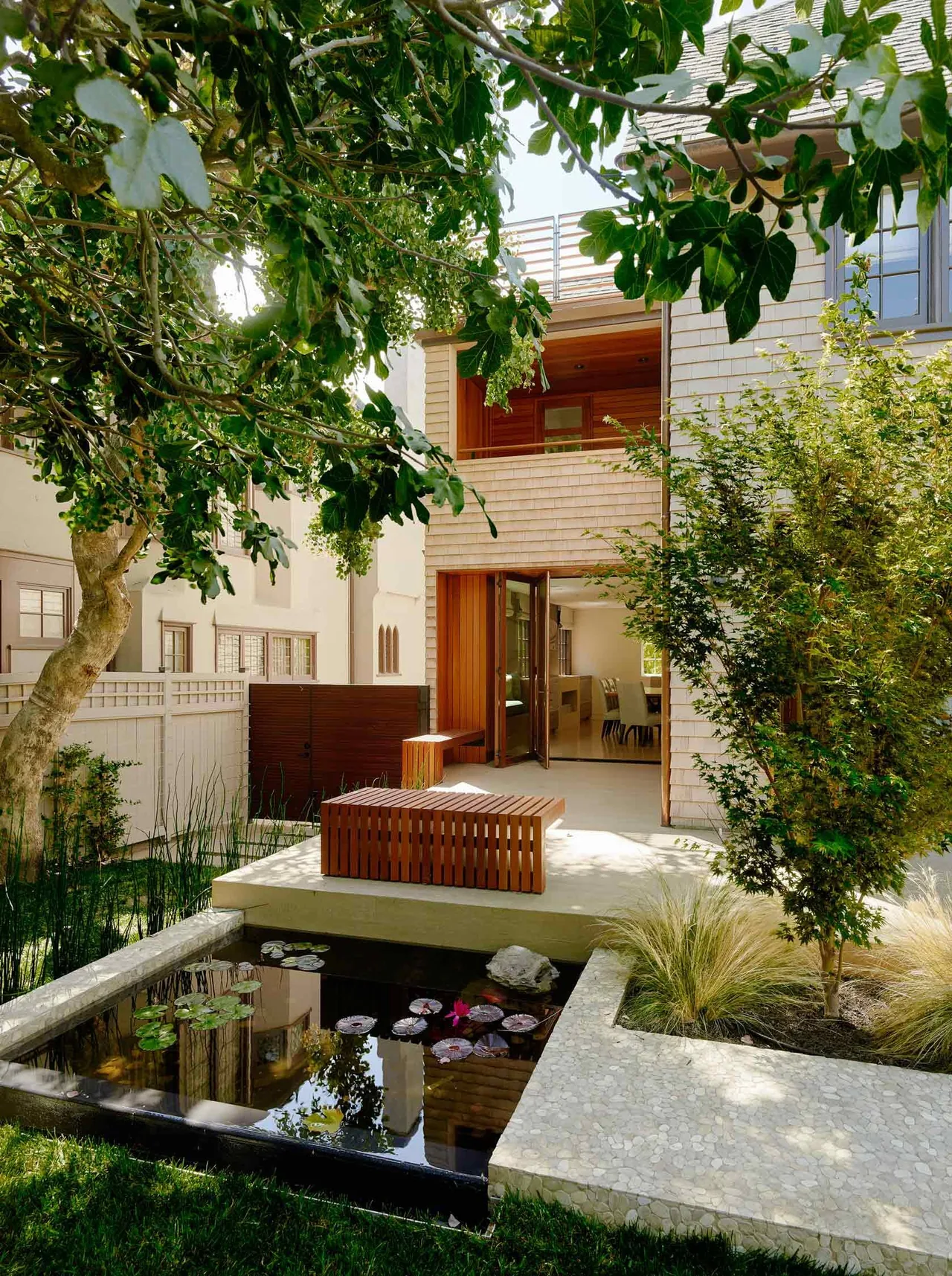 The Claremont Residence has a landscaped yard with a reflective pond, wooden benches, and a modern exterior with shingle siding.