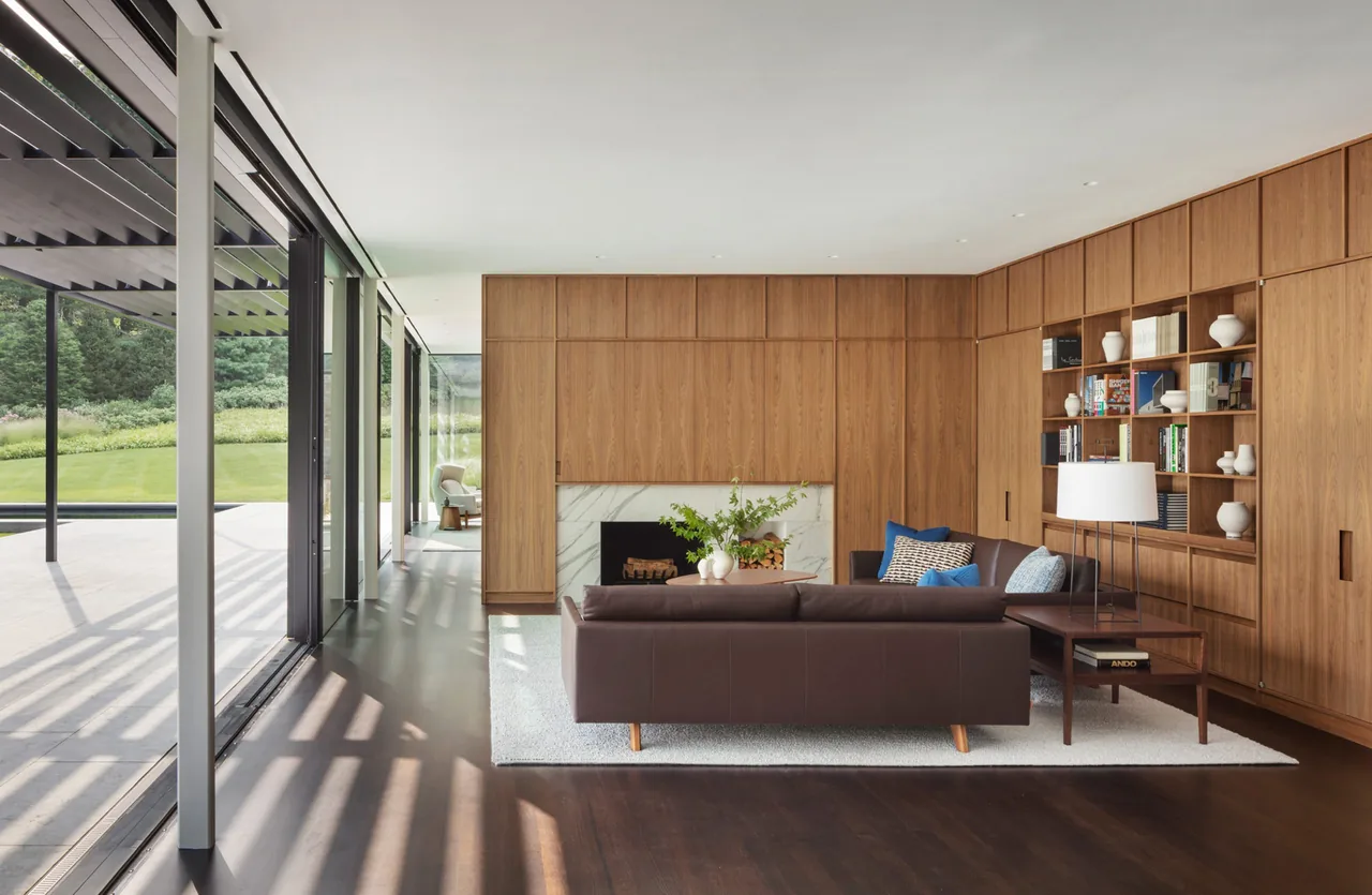 Living room features floor-to-ceiling windows, wood paneling with built-in shelves, a leather sofa, and a marble fireplace surround.