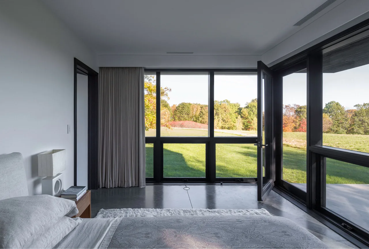 Sackett Hill House bedroom features black window frames and large floor-to-ceiling glazing overlooking the landscape.