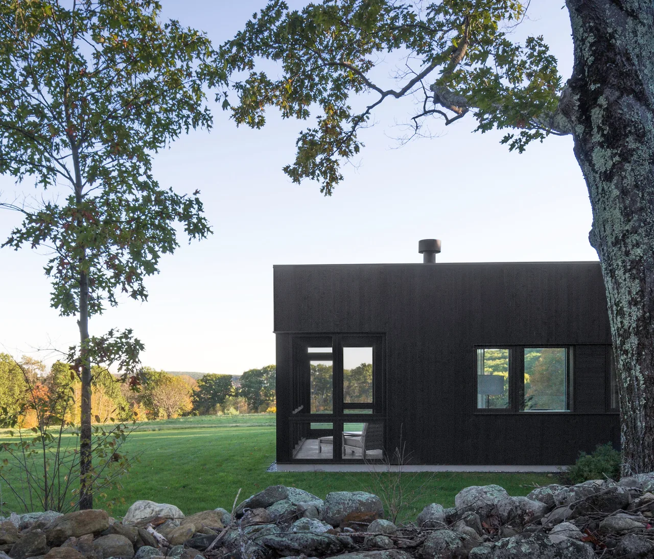 Sackett Hill House features black wood siding and rectangular windows overlooking a grassy field.