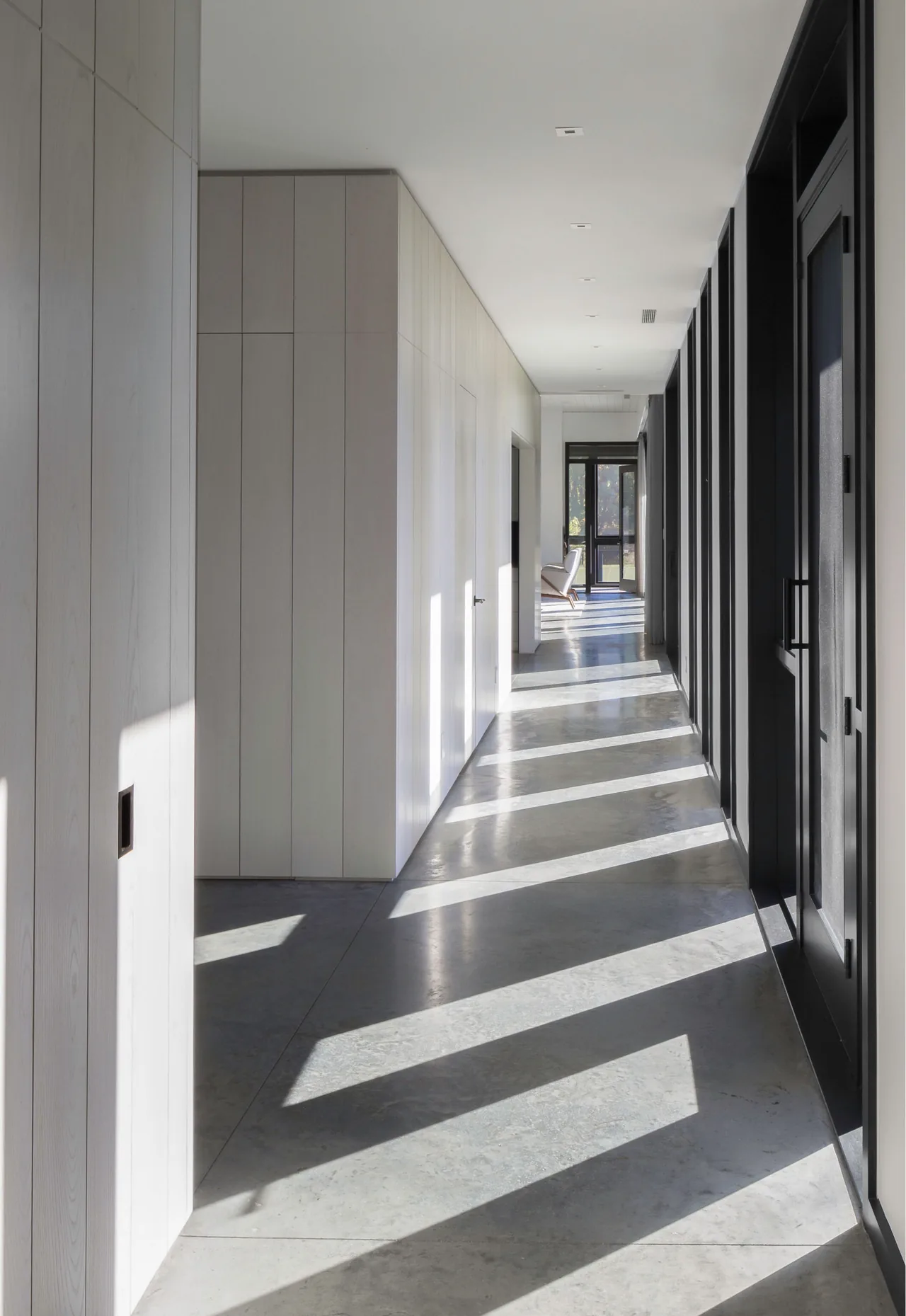 Hallway in Sackett Hill House features concrete floors, light wood-paneled walls, and black window and door frames.