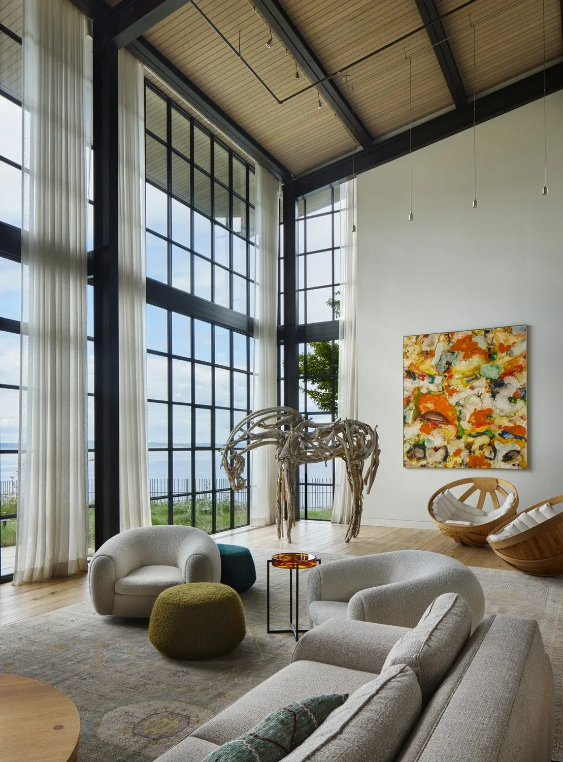 Living room in 'The Bluff' project features floor-to-ceiling grid windows with black frames and a sculptural driftwood horse art piece.