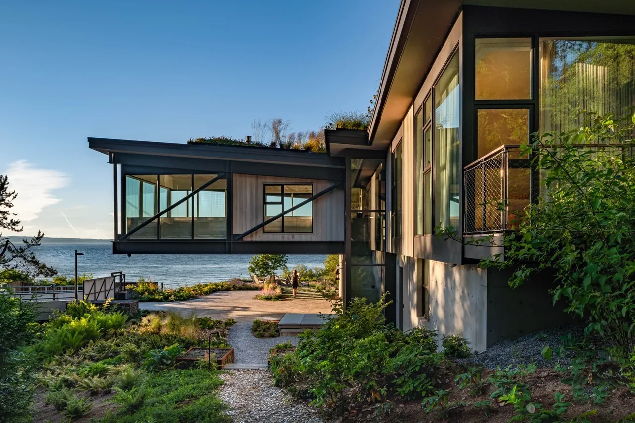 The Bluff features a cantilevered exterior room with floor-to-ceiling glass windows and a green roof, facing a waterfront view.