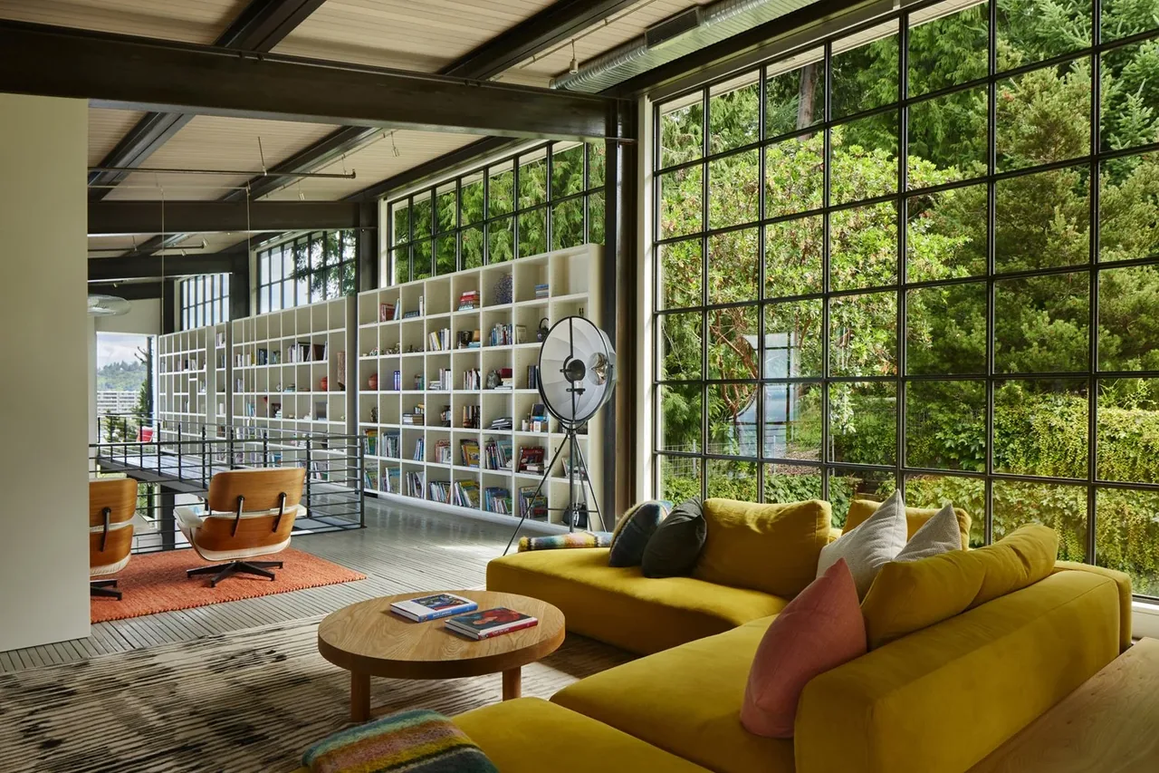 Living area features black-framed grid windows, a yellow sectional sofa, and built-in shelving, designed for The Bluff project.
