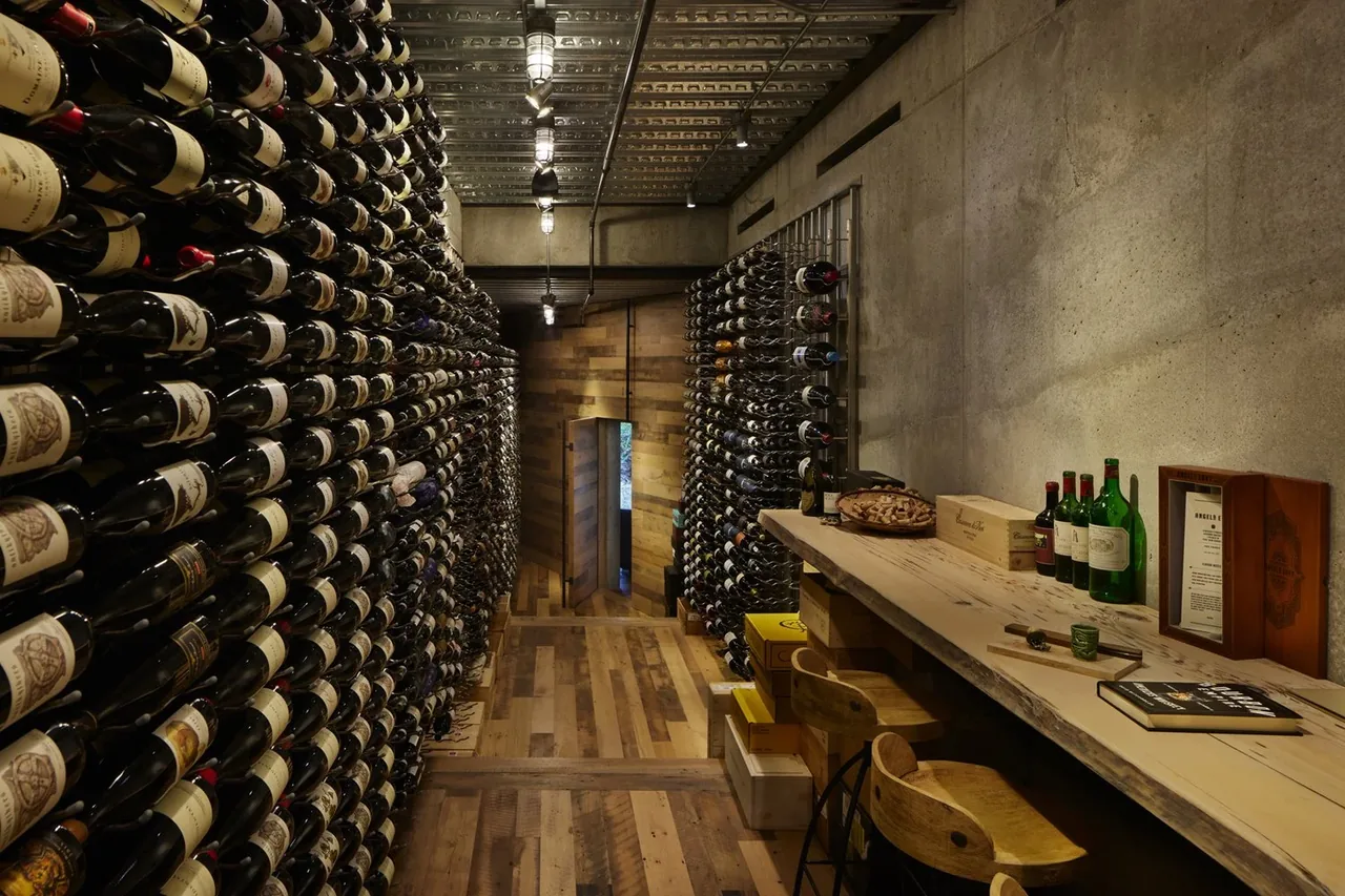 Wine cellar with wood flooring, concrete walls, and metal wine racks storing bottles horizontally on both sides.