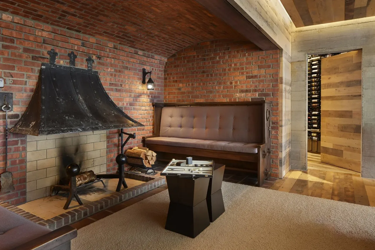 Room in The Bluff project featuring a vaulted brick ceiling with a blackened steel fireplace hood and tufted wooden bench.