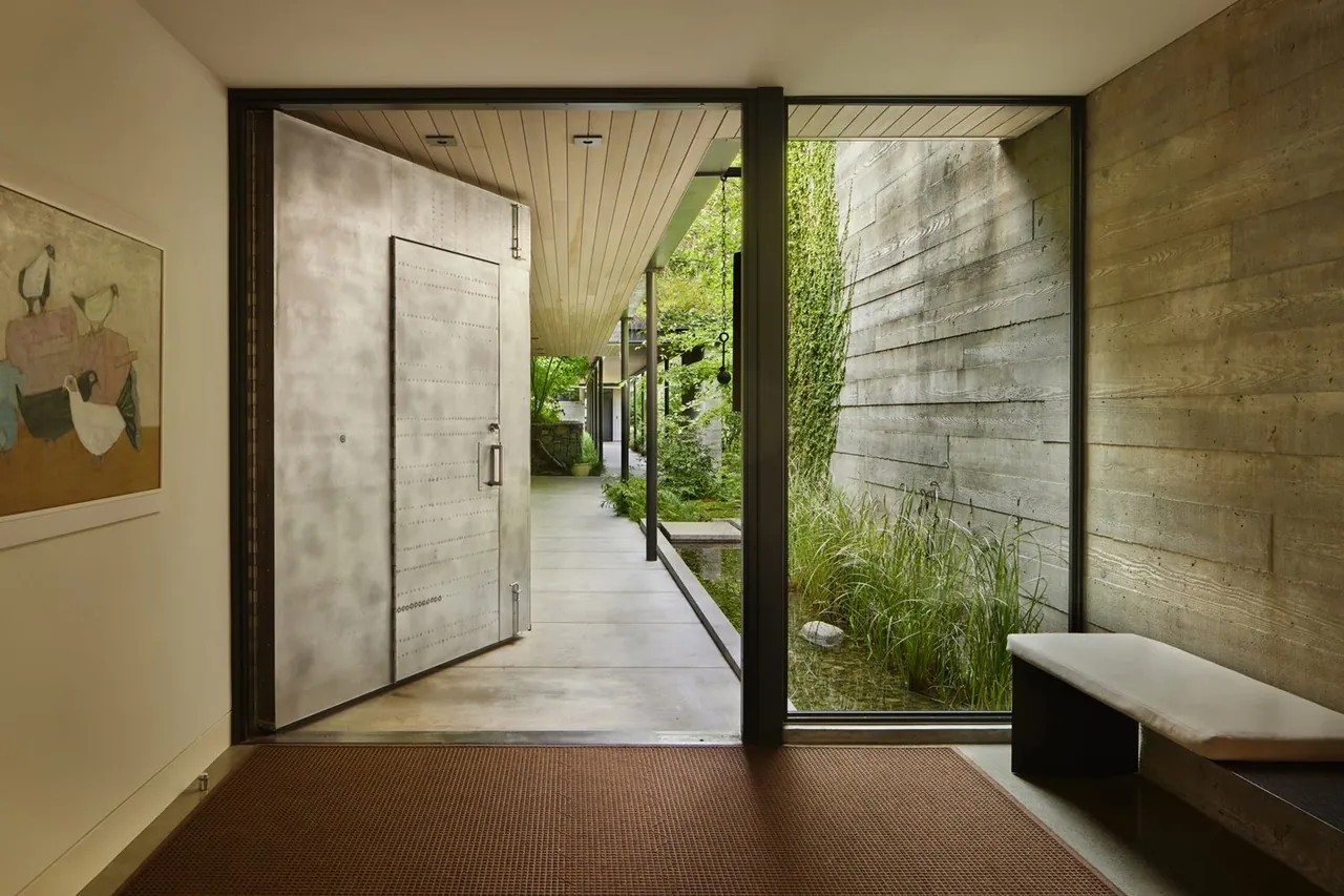 Entryway of The Bluff showing a riveted metal door opening to a planted courtyard with concrete walls and floor-to-ceiling glazing.