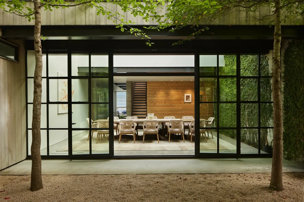 Dining room seen through large grid window walls with black frames and a wood-paneled wall interior at The Bluff project.