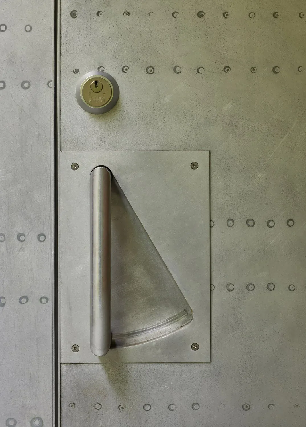 Detail of a metal door featuring a vertical cylindrical handle and circular key lock.