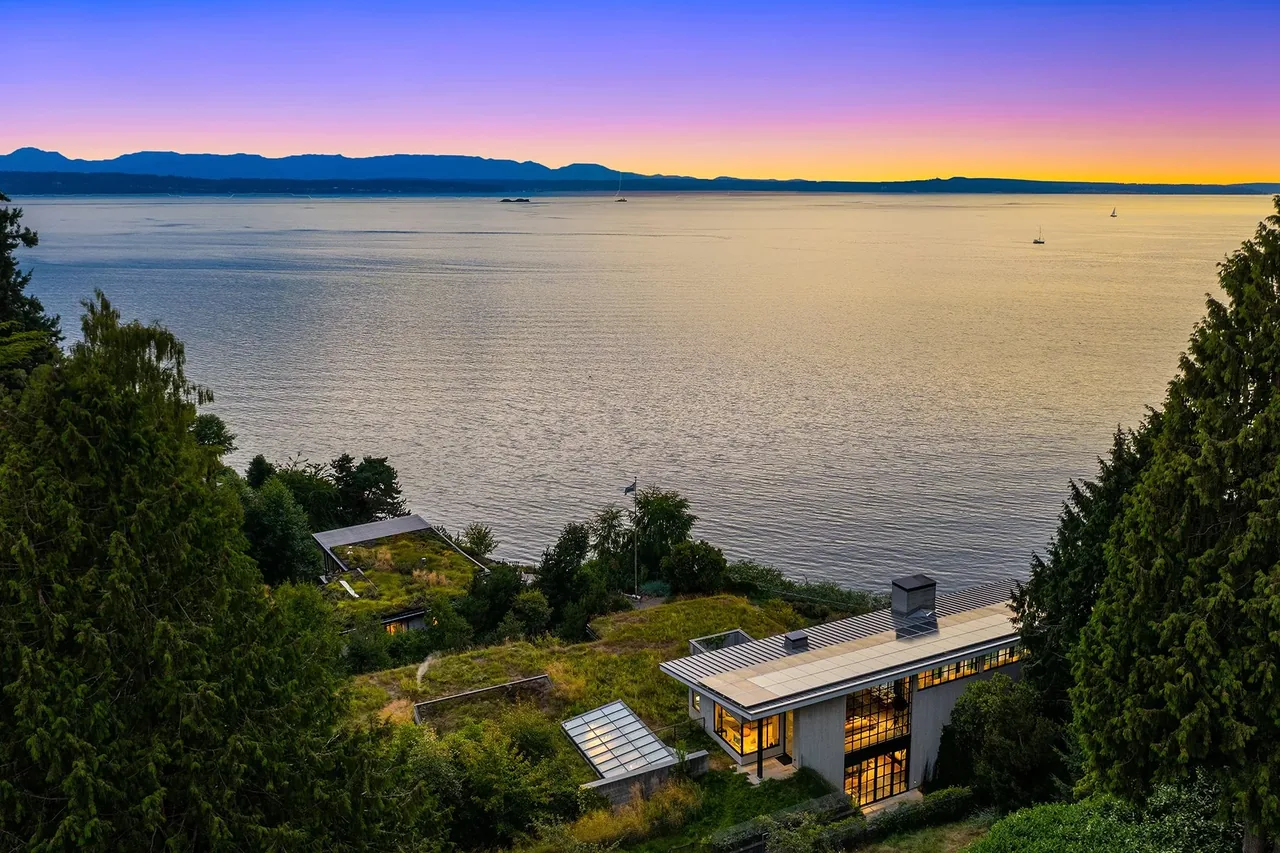 The Bluff features a modern house with a flat roof and extensive glazing overlooking the water during sunset.