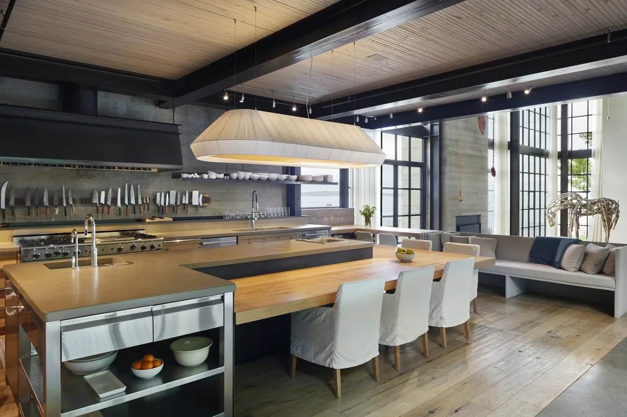 Open-plan kitchen and dining area featuring a large wood table, concrete countertops, and black-framed grid windows.