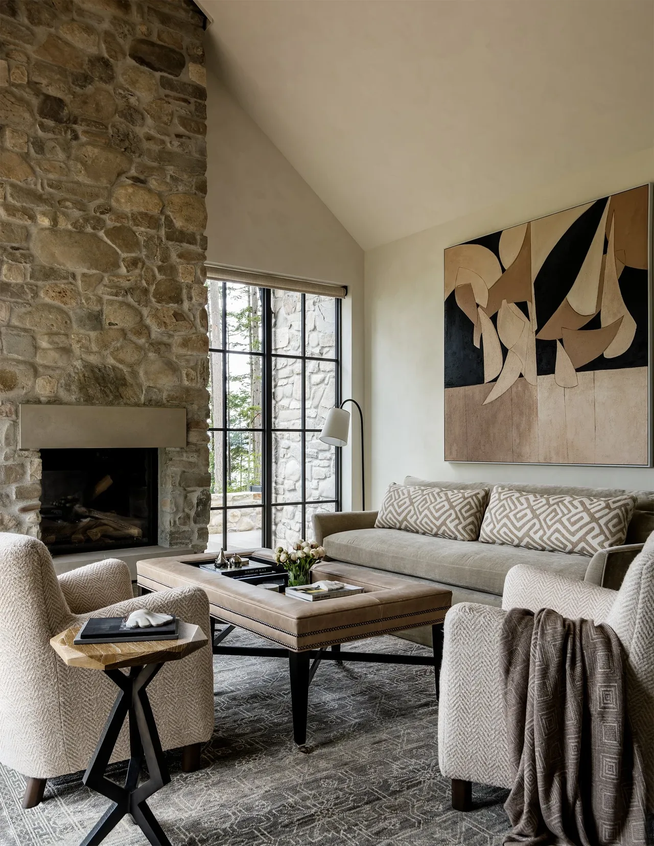 Keystone Cottage living room features a stone fireplace, black window frames, and a vaulted ceiling by DeForest Architects.