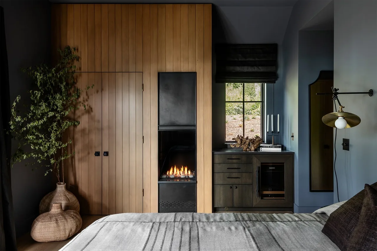 Keystone Cottage bedroom features a wood-paneled wall with a modern built-in fireplace and dark wood cabinetry under the window.