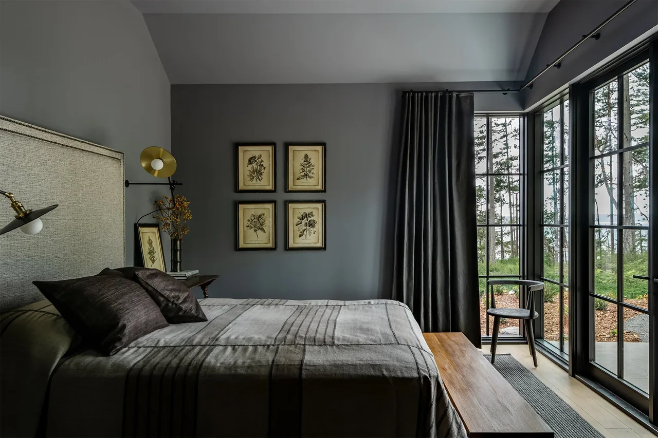 Bedroom with black-framed floor-to-ceiling windows presents a forest view at Keystone Cottage by DeForest Architects.
