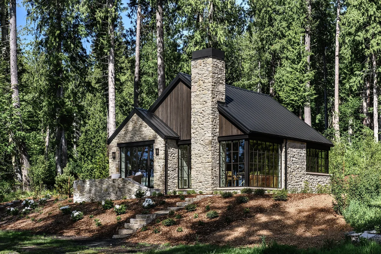 Keystone Cottage features a stone exterior with large windows and a tall stone chimney in its forest setting.