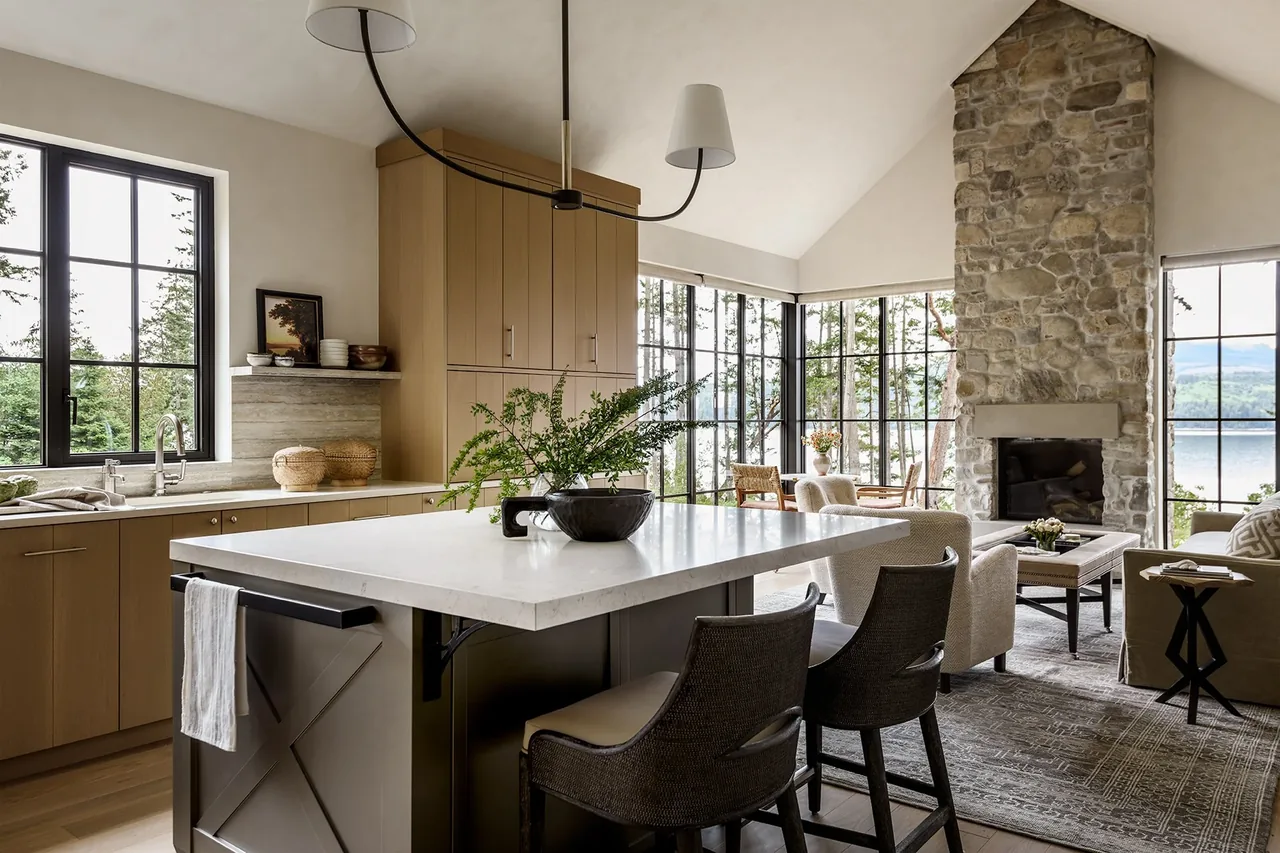 Keystone Cottage kitchen and living area feature a stone fireplace, large windows, vaulted ceiling, and a central island with seating.