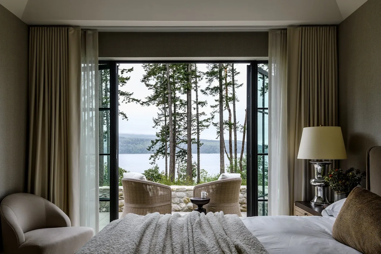 Bedroom opens to an outdoor patio with seating overlooking trees and a water view.
