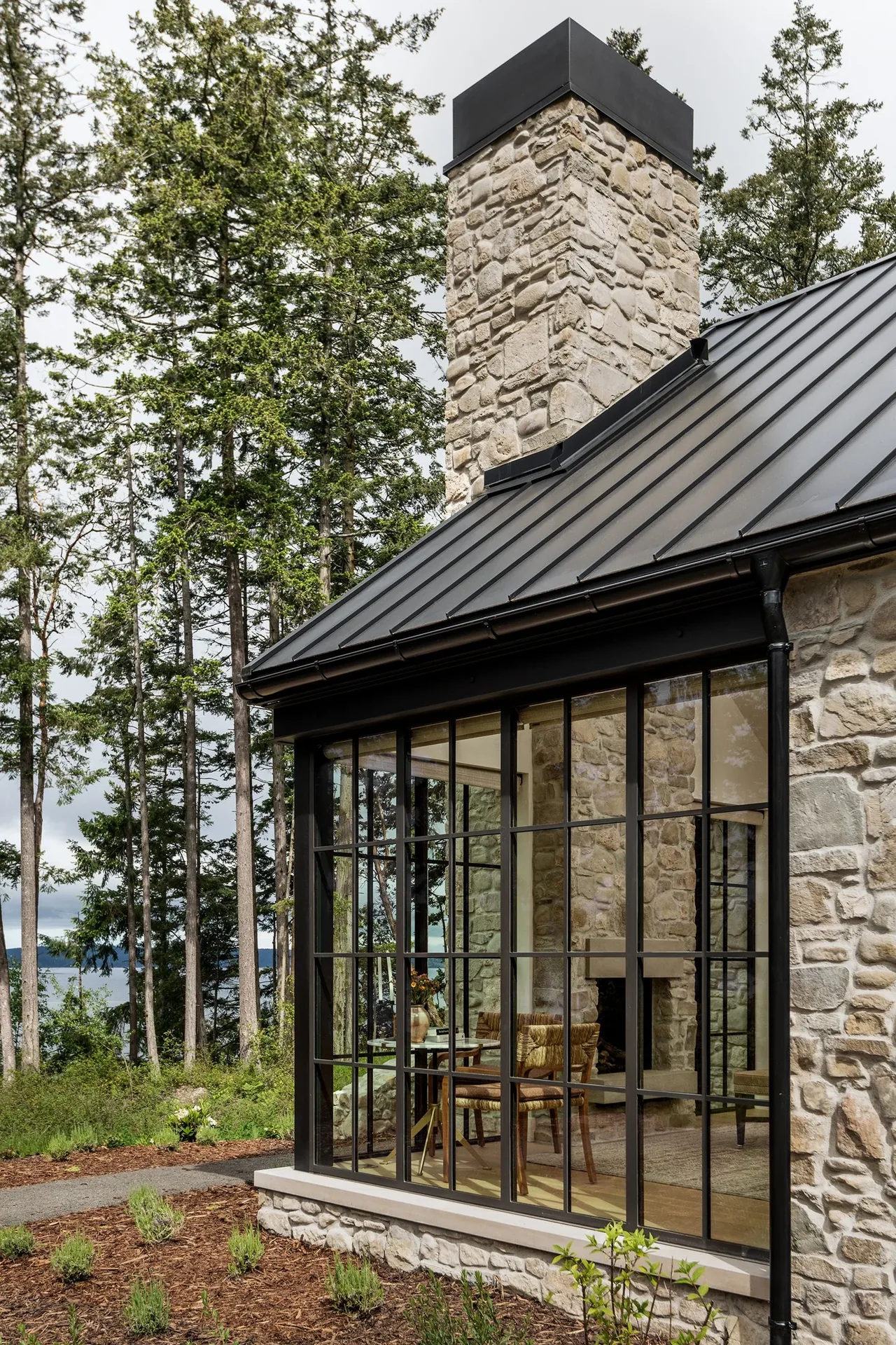 Keystone Cottage features a stone exterior with large grid windows and a standing seam metal roof by DeForest Architects in Seattle.