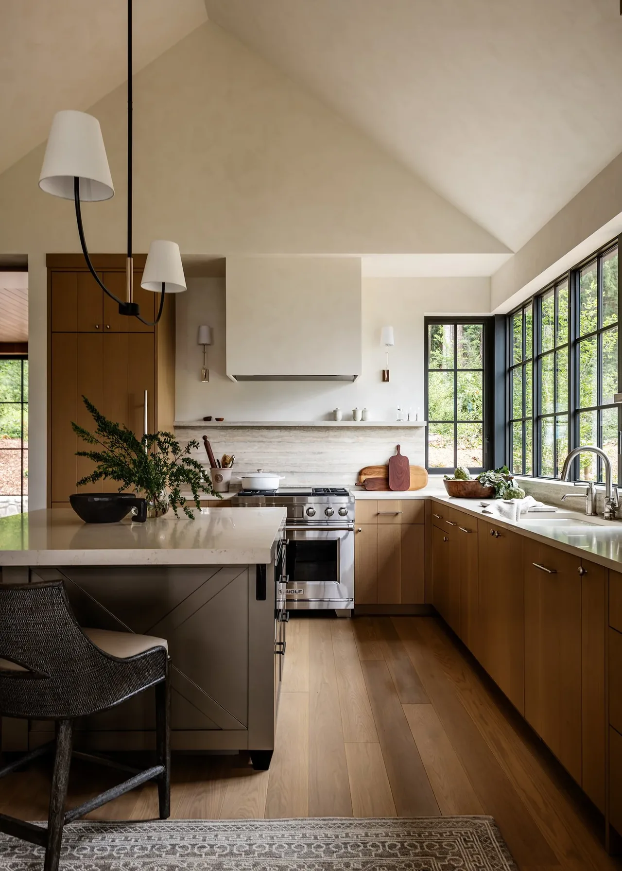 Keystone Cottage kitchen by DeForest Architects features wood cabinetry and vaulted ceilings with expansive black window frames.
