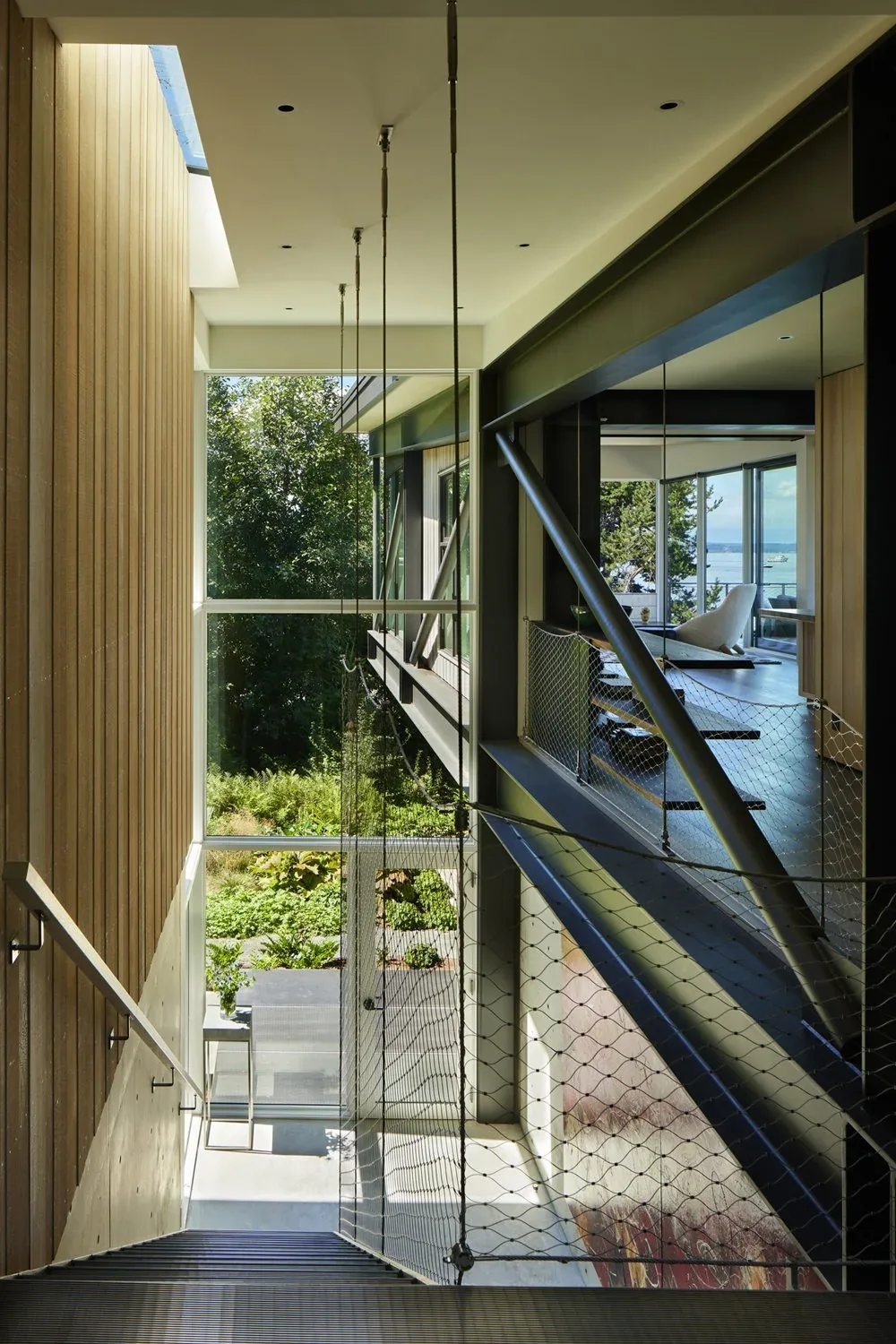 Stairwell with wood siding, glass window wall, and metal framing in Creek House by DeForest Architects.