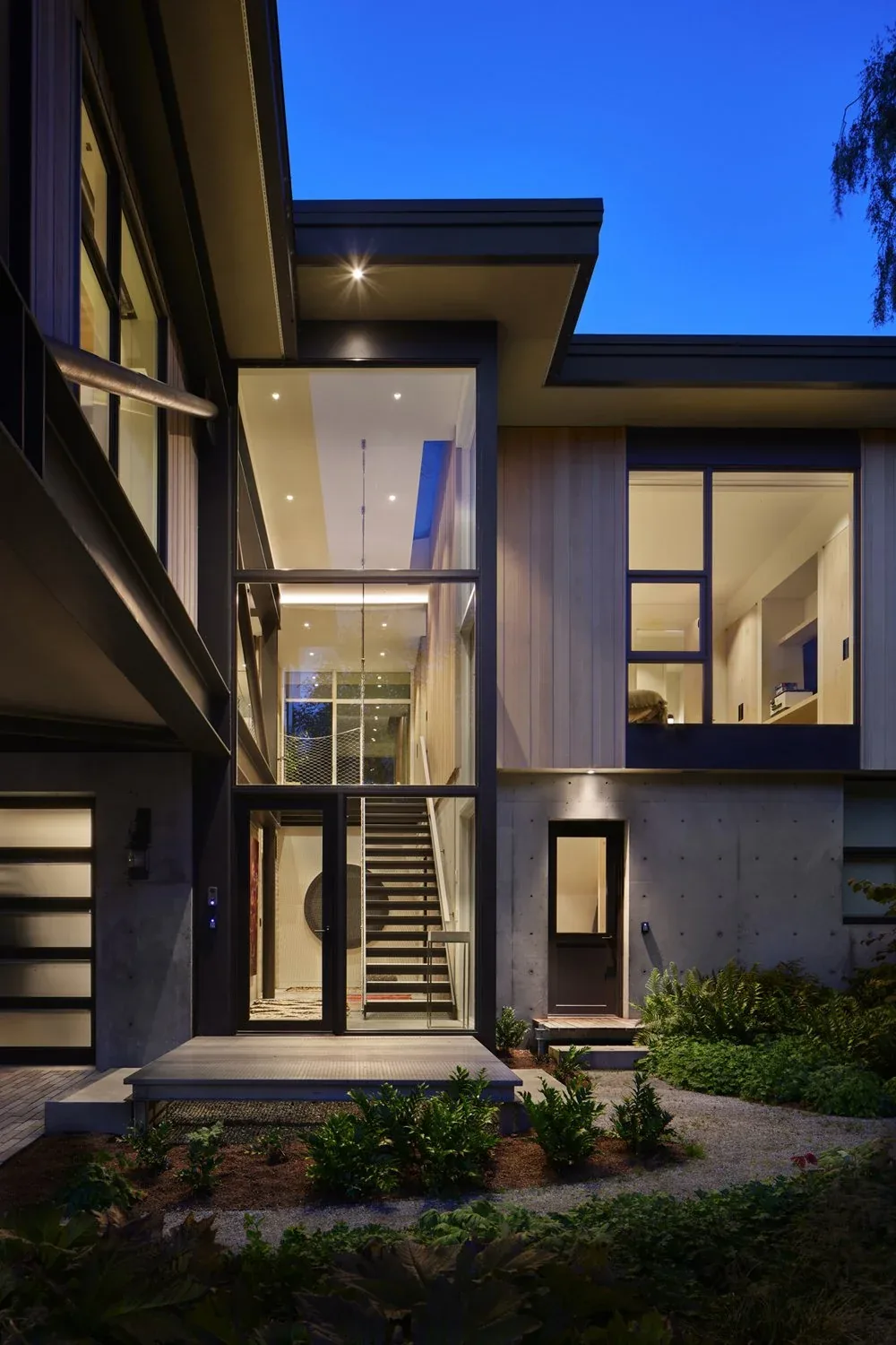 Creek House features a modern exterior with expansive floor-to-ceiling glazing revealing a stairway inside.