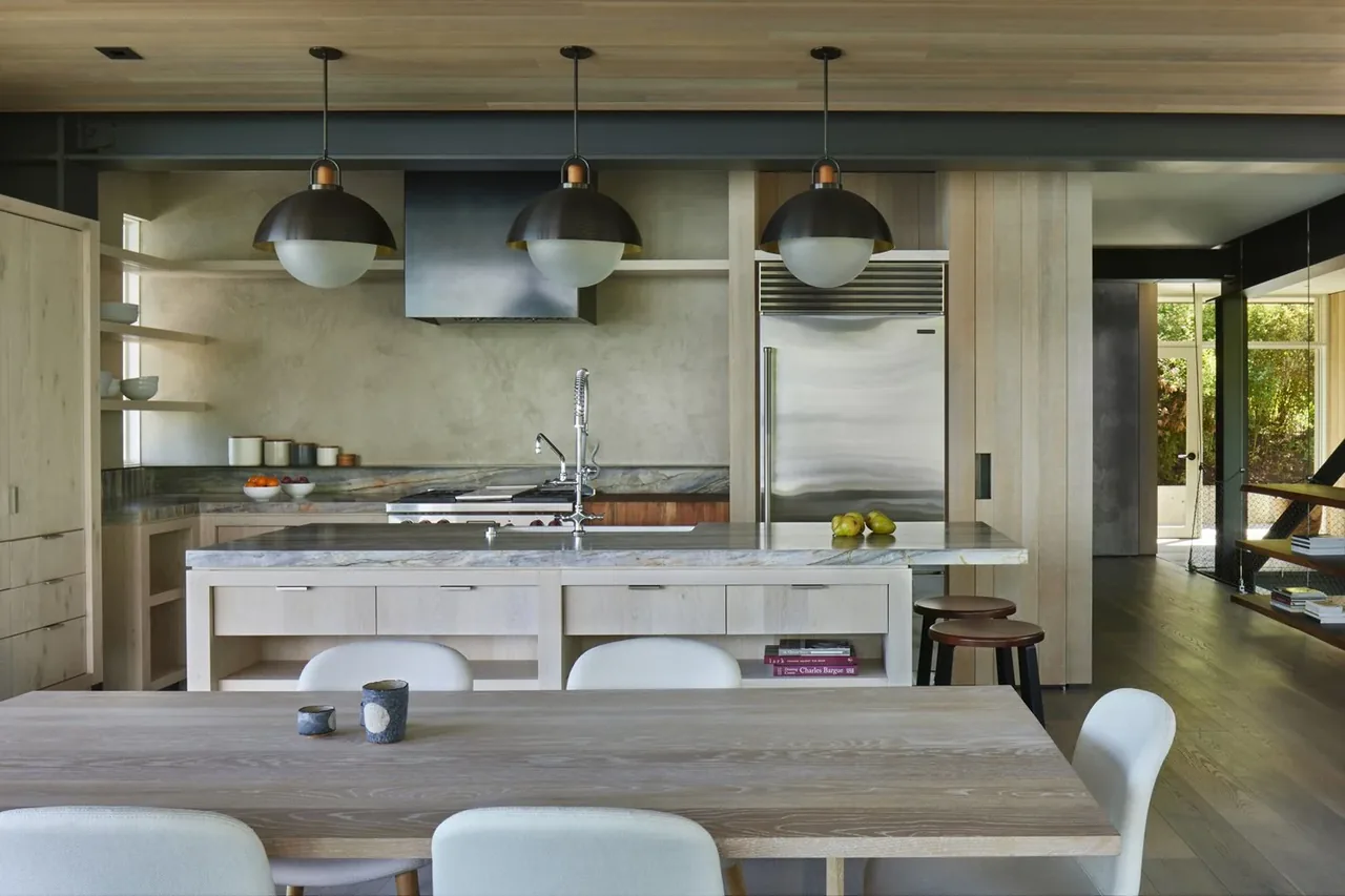 Kitchen and dining space of the Creek House featuring light wood finishes, marble countertops, and black pendant lighting.