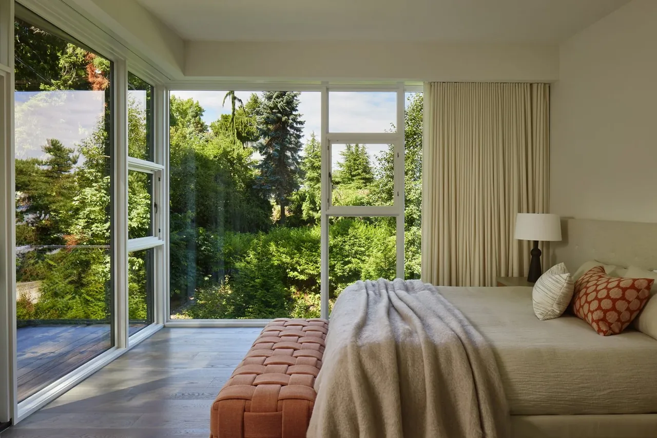 A bedroom featuring floor-to-ceiling corner windows provides abundant natural light and garden views.